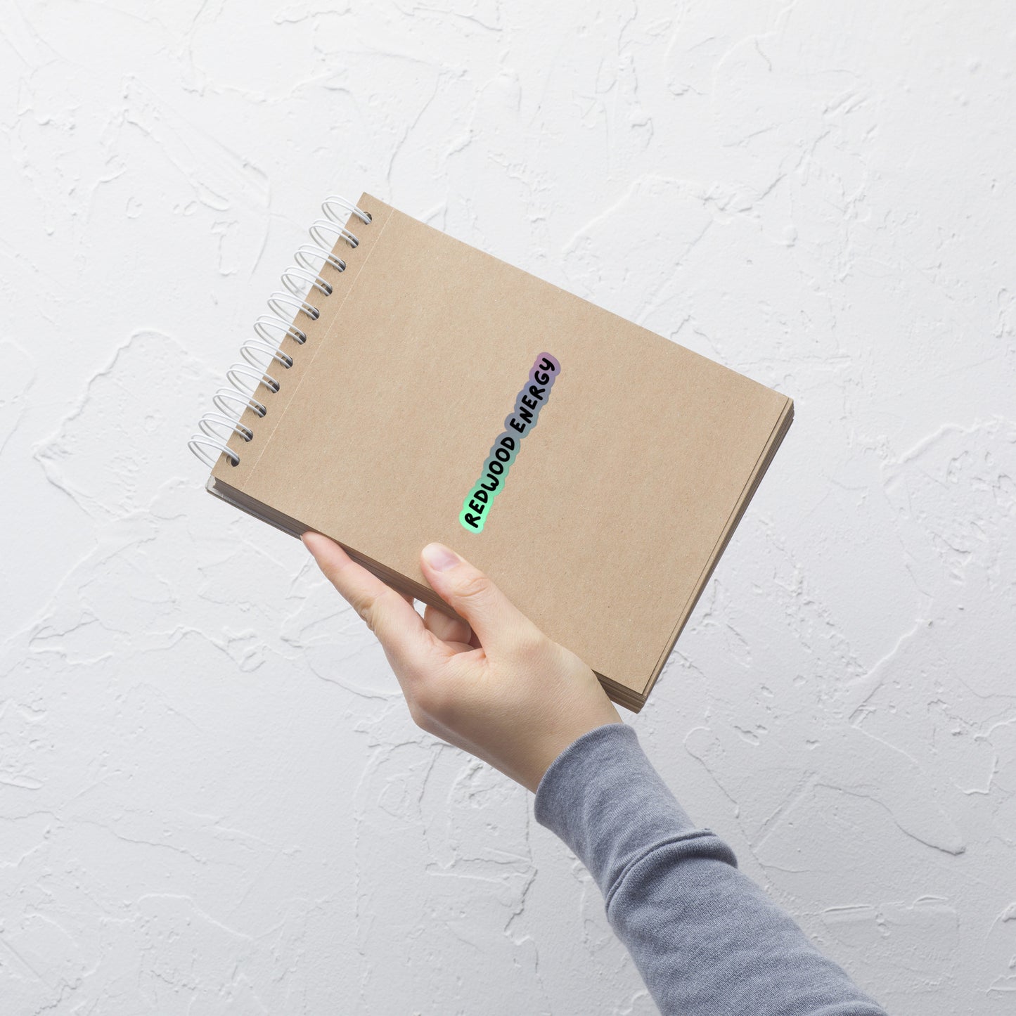 Hand holding a brown notebook with colorful stickers on a light gray background
