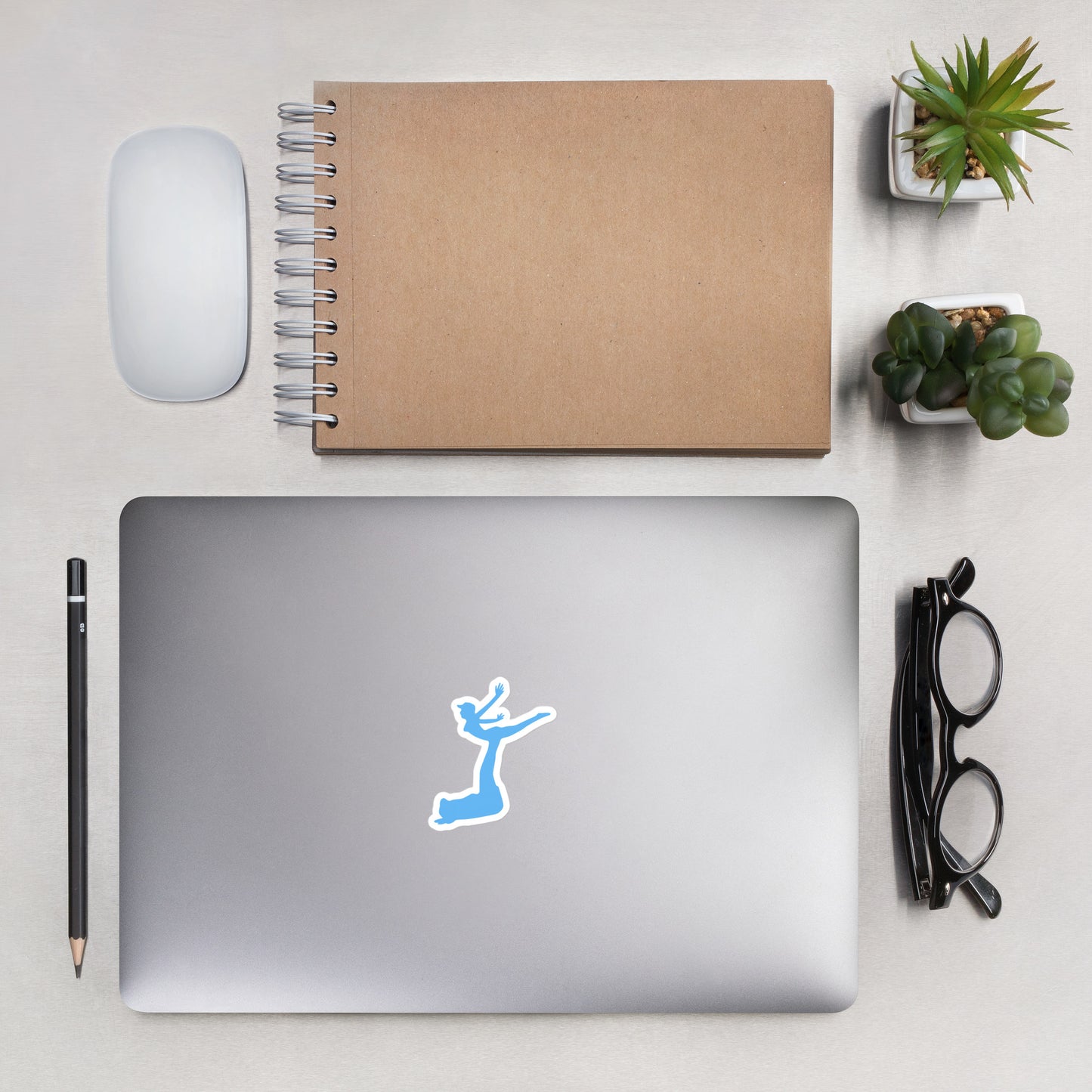 Air Jordon Logo of a man holding a woman in blue stuck to a laptop with a pen, glasses, mouse, notepad, and two small desk plants surrrounding the laptop.