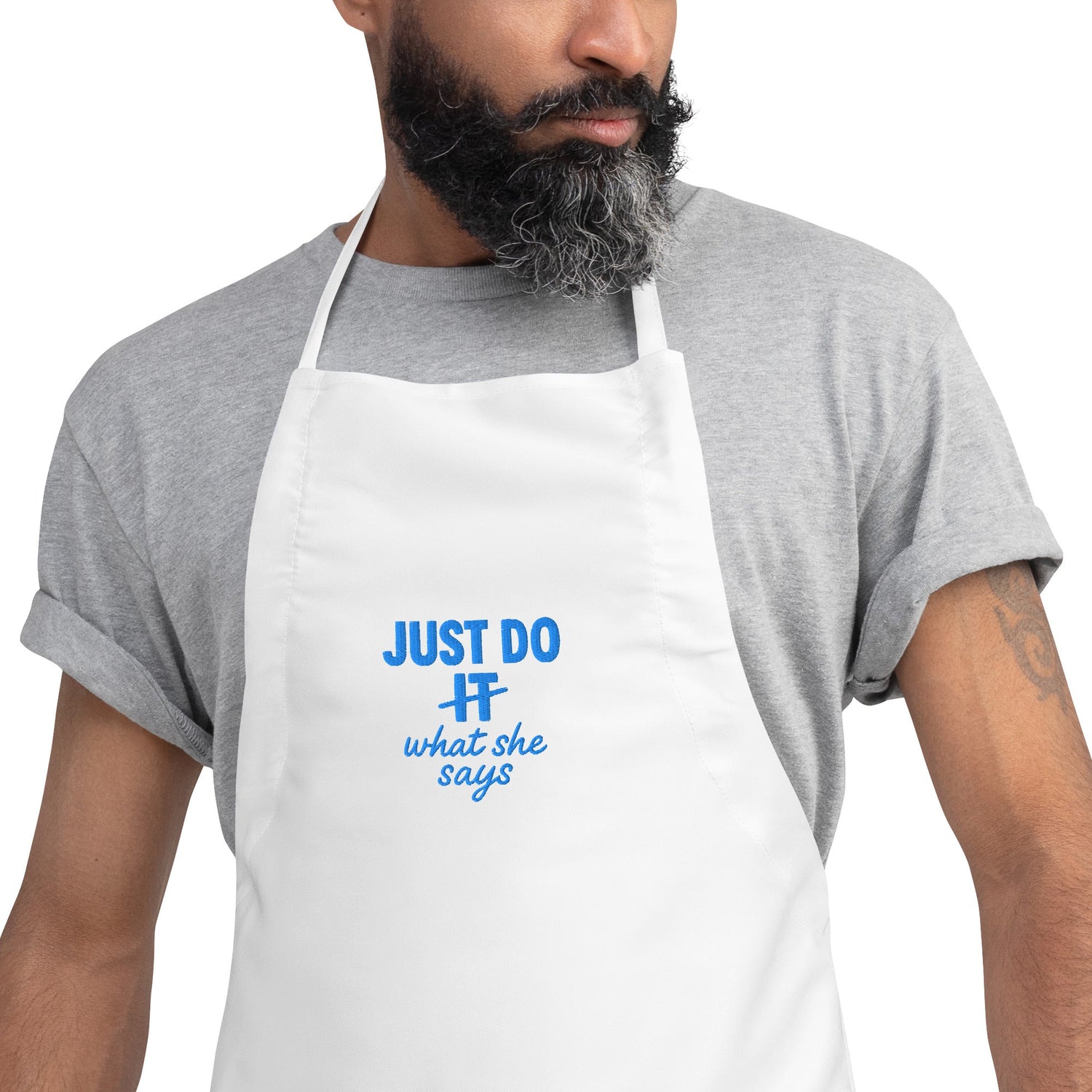 A man with a beard wearing a white apron that says Just Do What She says