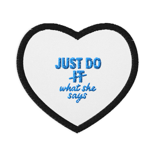 White heart patch with black outline and Just Do What She Says embroidered on the middle in light blue.