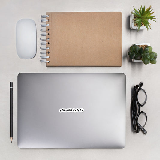 Laptop with 'Redwood Energy' sticker on a desk with notebook, mouse, pen, and plants.